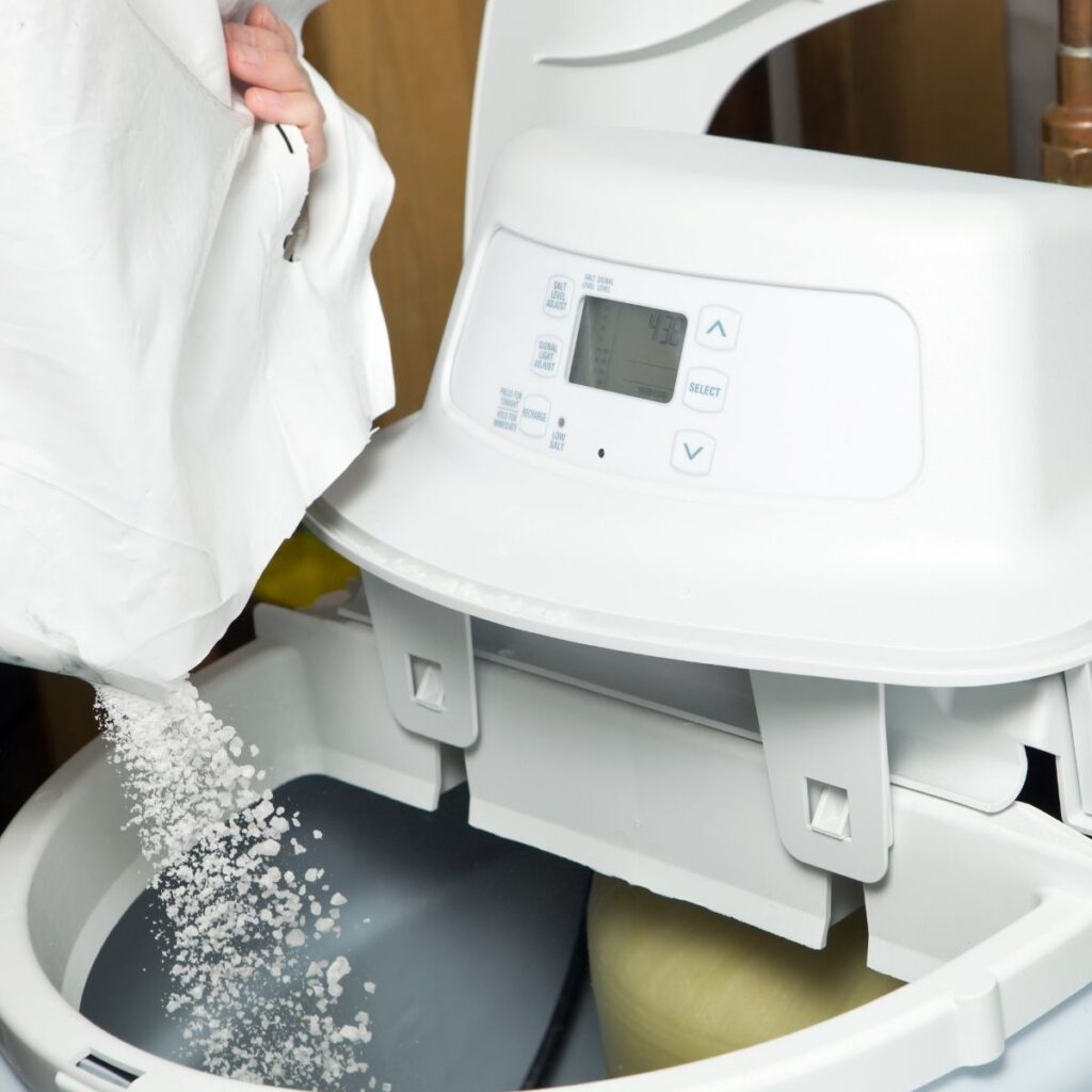 A close-up of someone pouring a white powdered substance into the water compartment of a high-efficiency water softening system