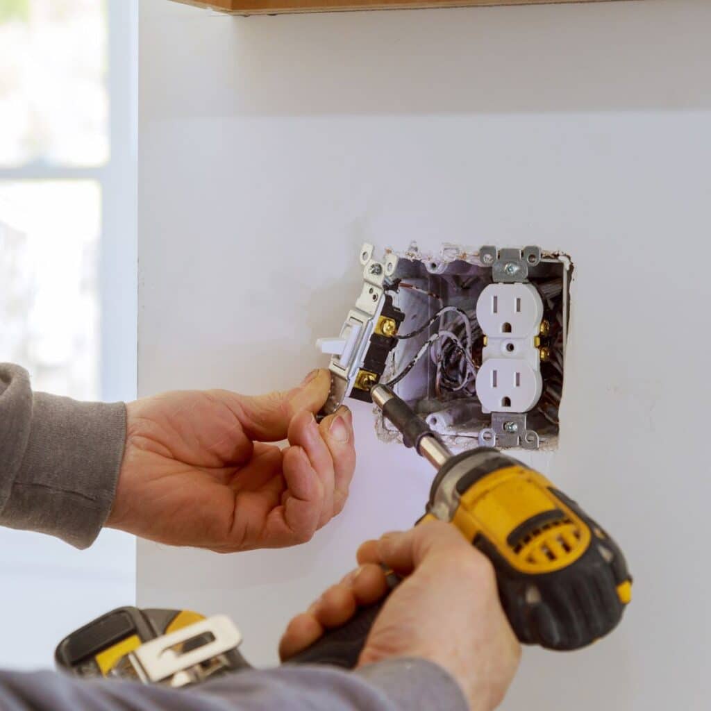 Electrician installing or repairing a wall outlet using a power drill, highlighting attention to safe electrical work