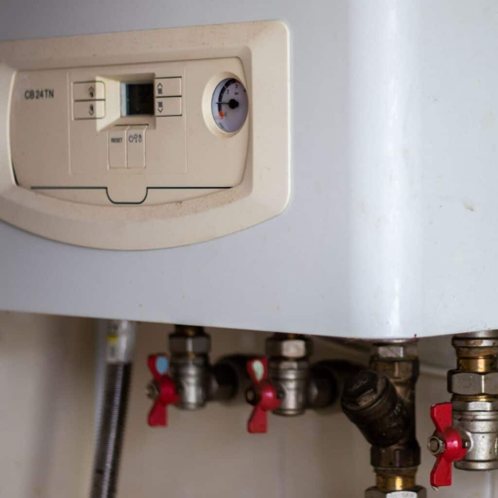 closeup of the bottom of a tankless water heater, showing the buttons and gauges on the system as well as the pipes underneath