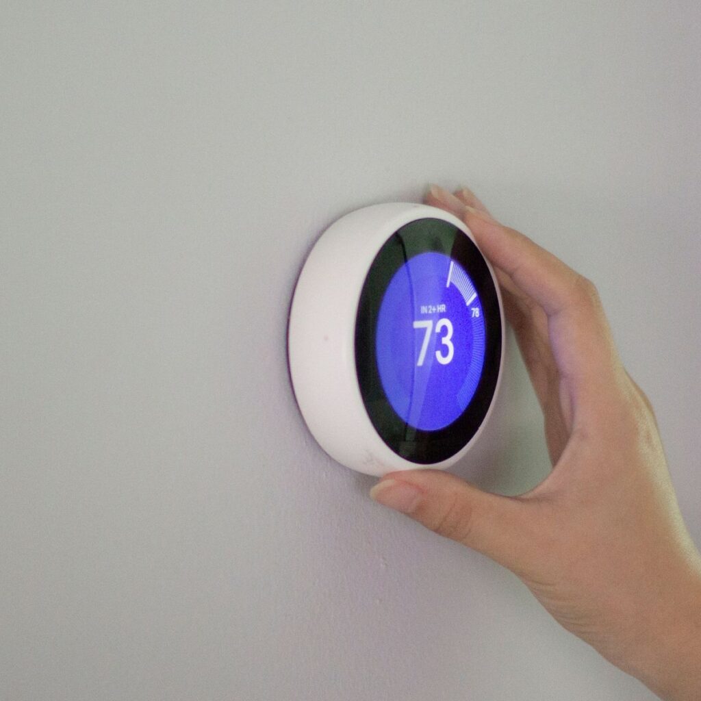 hand turning a smart thermostat that is showing 73 degrees on the screen