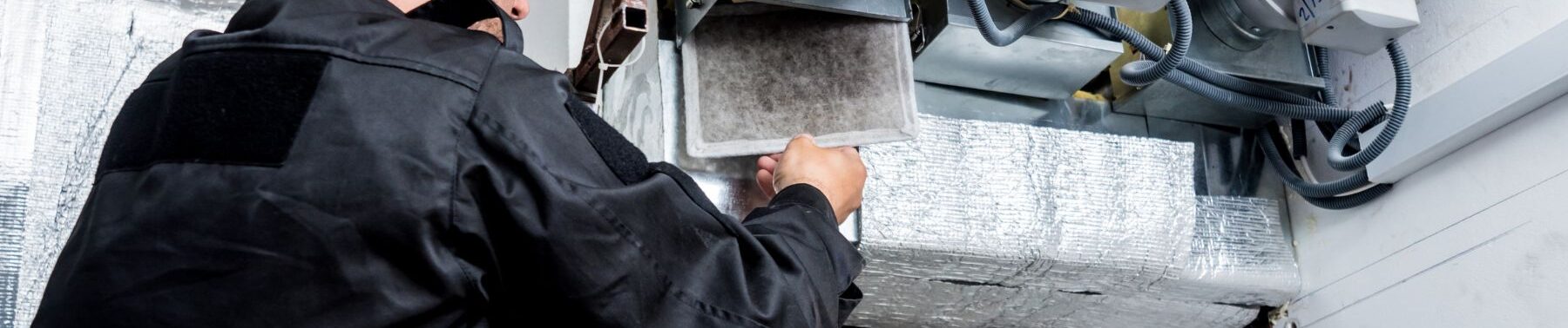 The back view of a technician, focused on replacing or cleaning an air filter in an HVAC system. This is indicative of regular maintenance to ensure good air quality and system efficiency