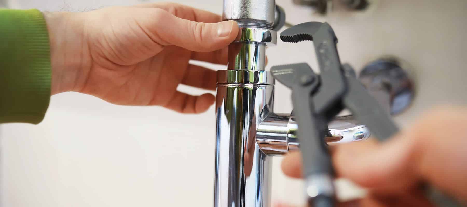 plumber using a wrench to perform repairs on a silver pipe under a sink