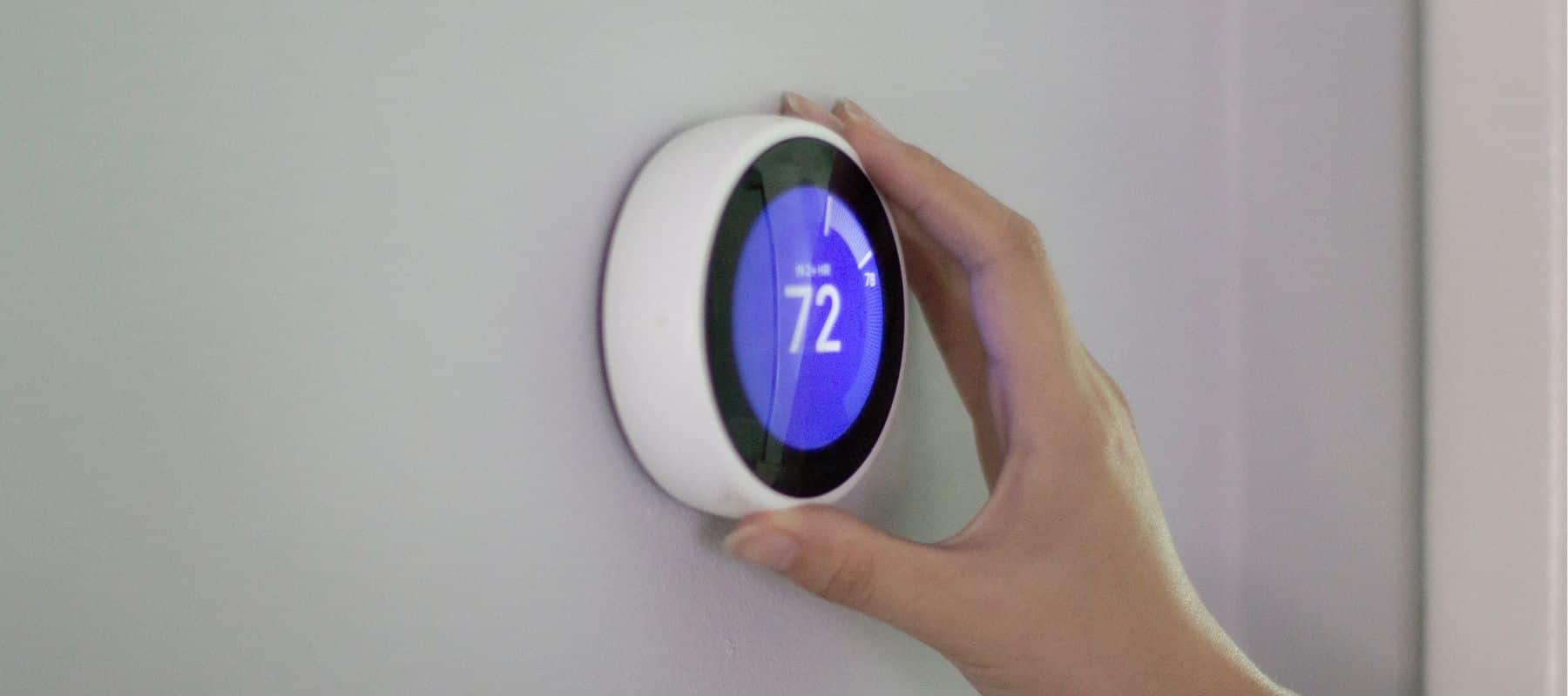 hand turning a smart thermostat that is showing 73 degrees on the screen