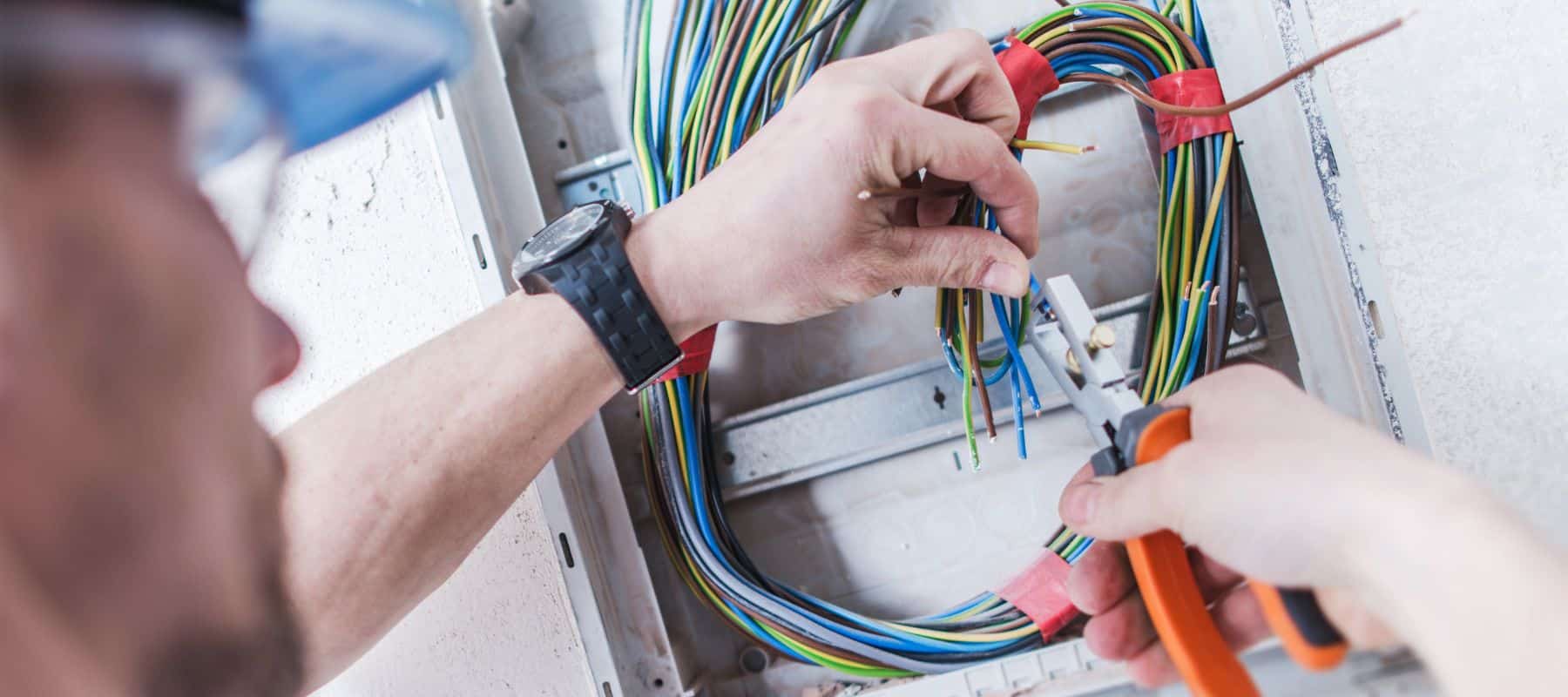 electrician using a clamp to perform repairs on colorful electrical wires in a electrical box