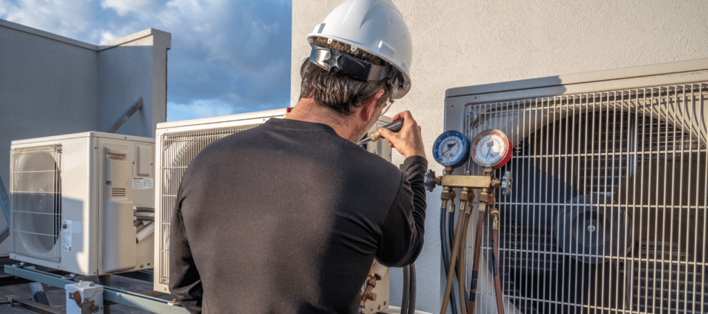 Technician tuning residential HVAC system for improved airflow and energy efficiency, Technician servicing residential outdoor AC unit beside an occupied suburban home