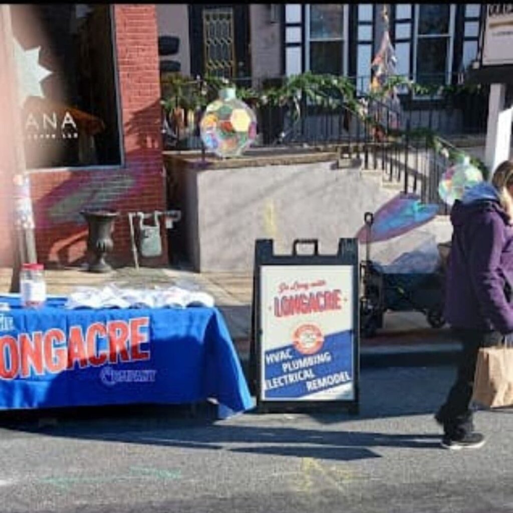 Street display booth with a Longacre Company table and sign promoting HVAC, plumbing, electrical, and remodeling services
