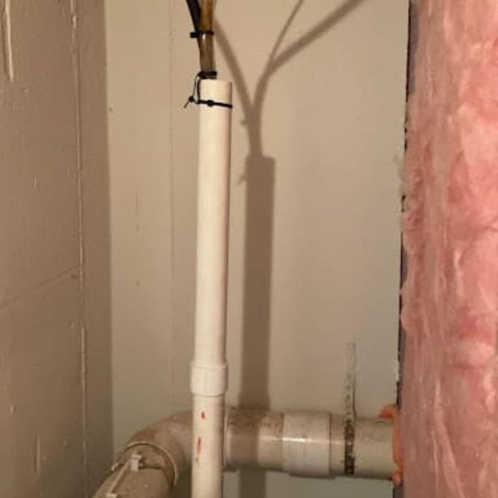 White PVC drainage pipe connected to horizontal plumbing behind a basement wall