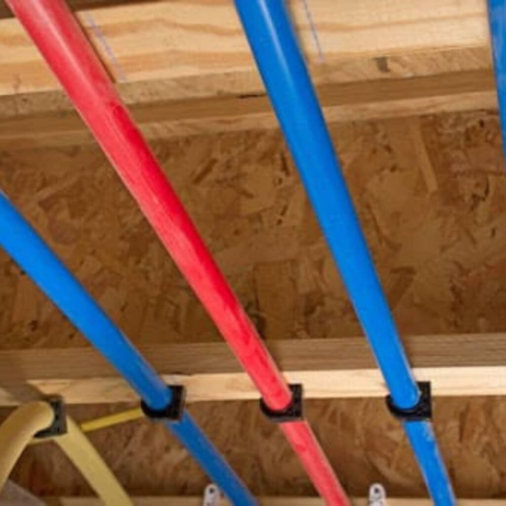 Red and blue PEX pipes installed along wooden ceiling joists in a repiping project
