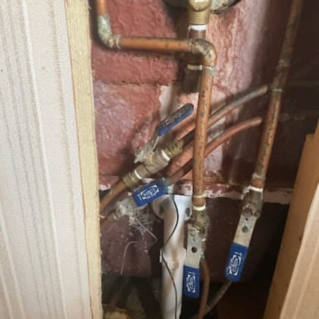 Exposed copper water pipes and valves connected to a residential plumbing system inside a wall