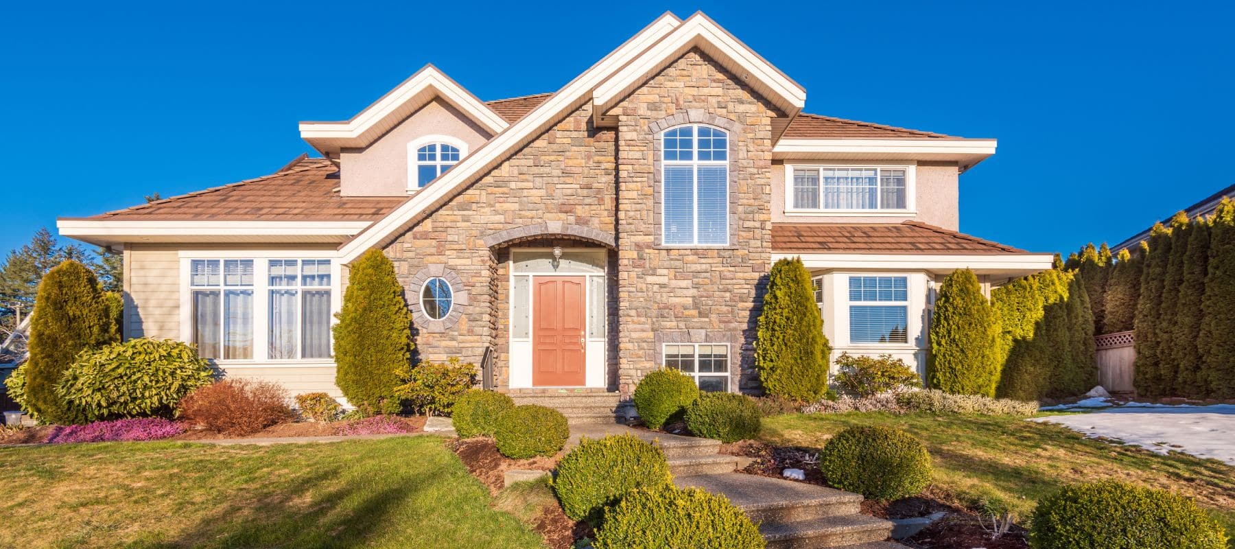 Brightly lit home featuring a brown shingle roof, stone veneer exterior, and a neatly landscaped yard