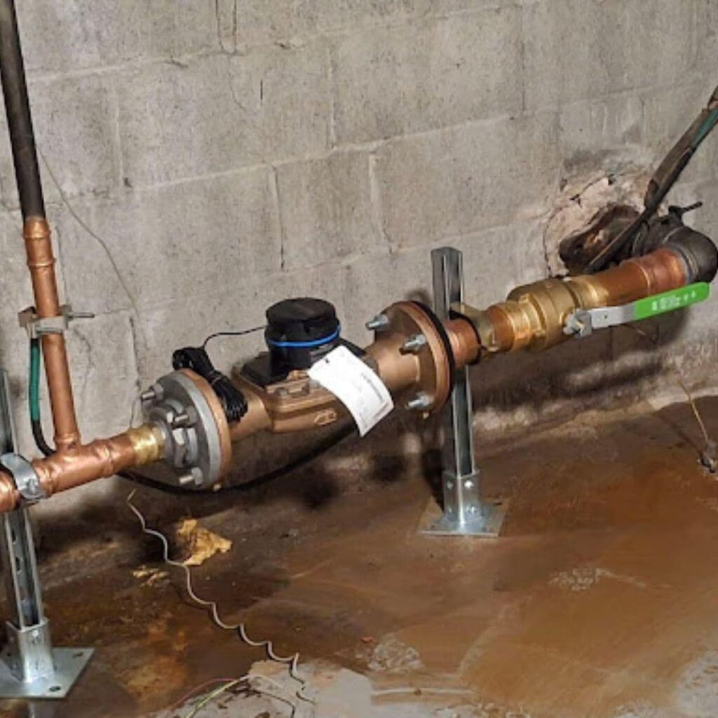 Close-up of a newly installed water meter and backflow prevention assembly mounted on concrete wall supports