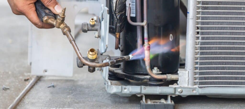 closeup of an hvac technician using a small blow torch to perform hvac repairs, Emergency HVAC technician troubleshooting furnace failure with diagnostic tools at night