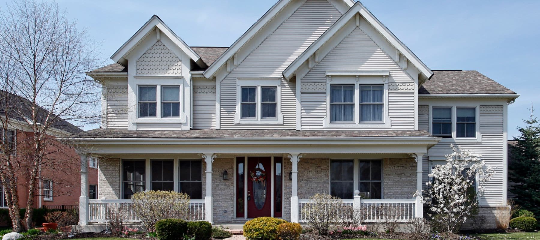 Two-story cream-colored suburban home with a red front door and landscaped front yard