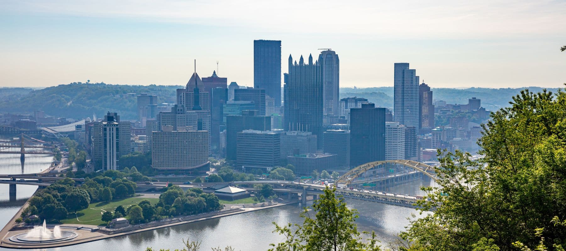 Skyline view of Pittsburgh, PA featuring its rivers, bridges, and tall downtown buildings on a hazy morning
