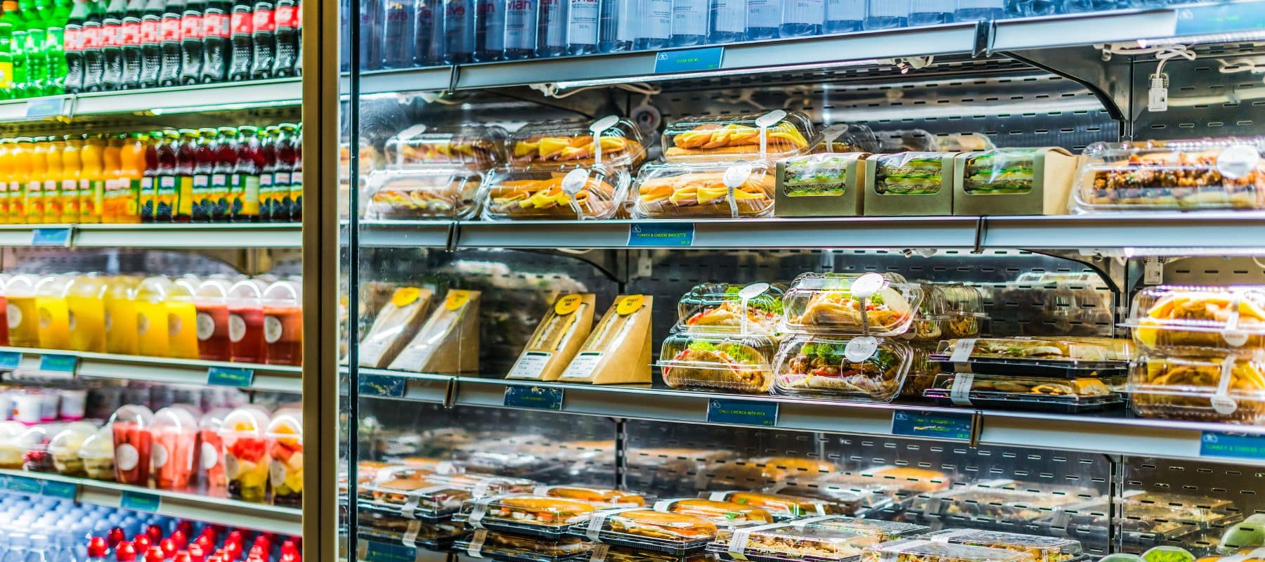 A commercial refrigerated display case is fully stocked with various pre-packaged sandwiches, salads, and drinks