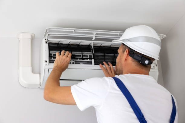 Technician diagnosing failed air conditioner at busy family home on hot afternoon, Technician repairing air conditioner at older Norristown home during summer afternoon